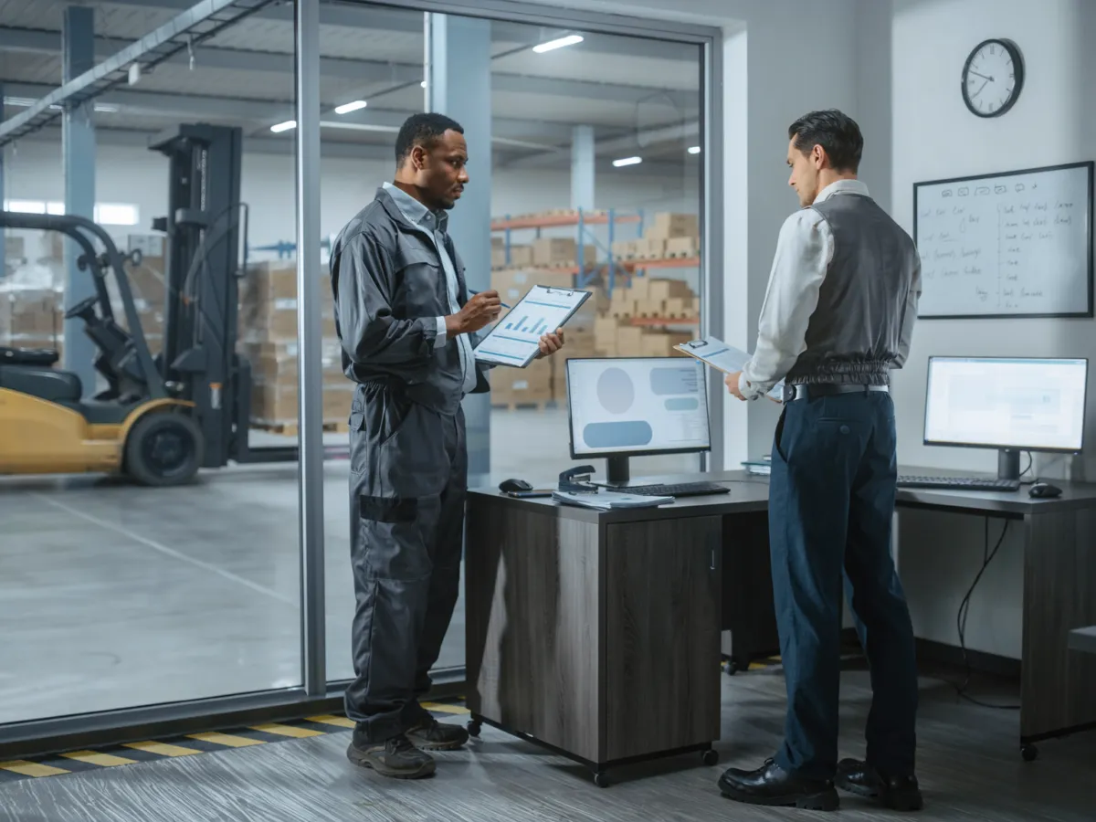 Conceptual AI-assisted editorial scene of workers in an industrial office beside a warehouse, illustrating business adoption of AI in developing Europe.