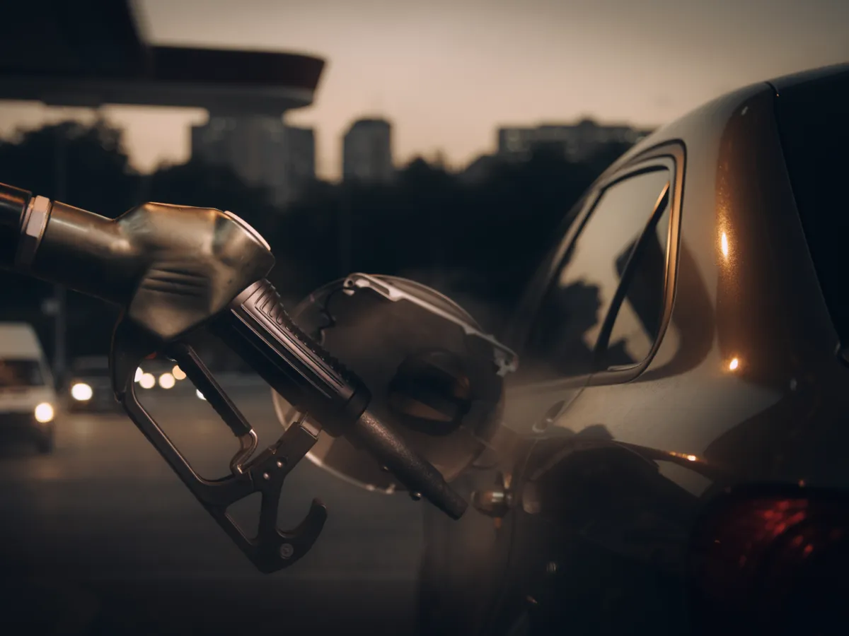 Conceptual editorial image of a gasoline pump beside a commuter car at a US filling station, illustrating fuel costs rather than a photographed news event.